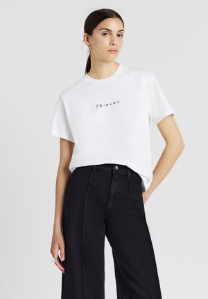 T-shirt bianca in cotone con collo tondo e maniche corte, che presenta la parola "FRIENDS" in lettere nere sul petto. Abbinata a pantaloni neri a vita alta.