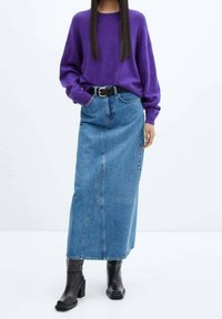 Woman wearing a purple sweater tucked into a high-waisted blue denim midi skirt with a black belt and black heeled boots.