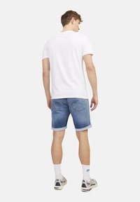 Men's outfit featuring a white cotton T-shirt, blue denim shorts with rolled cuffs, white socks, and gray athletic shoes.