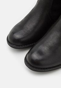 Bottes montantes en cuir noir avec une finition lisse, des bouts arrondis et des coutures visibles le long du bord des semelles.