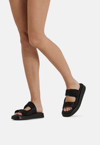 Sandali neri con cinturini testurizzati e dettagli brillanti. Sole piatto, design con punta aperta, chiusure regolabili in velcro per una vestibilità ideale.