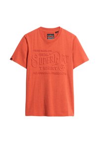 Red short-sleeve t-shirt made of cotton, featuring raised text logo "SUPERDRY" and additional branding on the front. Classic crew neckline.