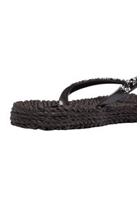 Sandale tong noire texturée avec semelle tissée et brides supérieures décorées sur fond blanc.