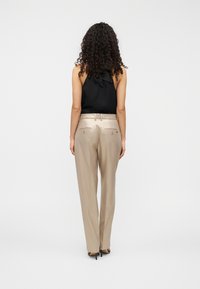 Μαύρο κορμάκι με ραβδώσεις και λεπτομέρεια φιόγκου στην πλάτη, σε συνδυασμό με ανοιχτό μπεζ παντελόνι σε εφαρμοστή γραμμή με κουμπιά και λεία υφή.