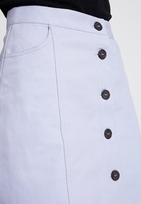 Ljusblå denimkjol med rak passform, med en rad bruna knappar framtill och sidofickor. Strukturerad tyg.
