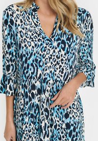 Blå leopardmönstrad klänning gjord av lättviktsmaterial. Har en v-ringning och 3/4 ärmar med volangfållar. Distinkt färgkontrast.