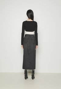 Top negro de manga larga cortado, superpuesto sobre una camisa blanca, acompañado de una falda larga de mezclilla oscura de tiro alto y botas negras de tacón.