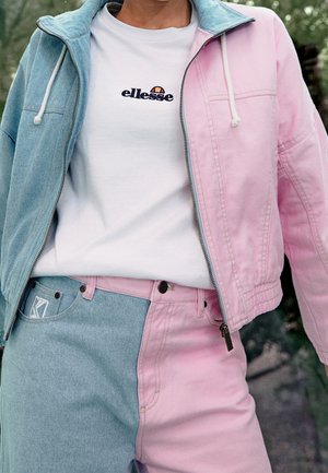 Jasnoniebieska i różowa dżinsowa kurtka z zapięciem na zamek, w połączeniu z pasującymi spodniami. Biała koszula z logo pod spodem, z kontrastującymi kolorami.