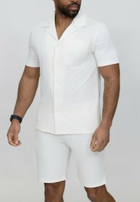 Chemise blanche à manches courtes et shorts assortis, texturés avec un subtil motif en zigzag. Boutons sur la chemise et poche incluse.