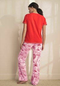 Red short-sleeve shirt with contrast stitching and relaxed fit, paired with pink pajama pants featuring red graphic patterns of fruits and designs.