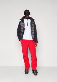 Skidragt med en grå og sort puffjakke, hvid base lag, lysrøde skibukser og sorte skistøvler. Glat tekstur, sporty design.