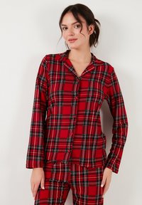Punainen ruudullinen pyjamapuku, jossa on pitkät hihat, napitus edessä, musta-valkoiset tarkkuudet, sileä kangaslaatu ja klassinen kaulus.