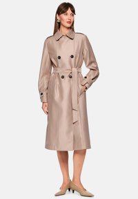 Beiger Satin-Trenchcoat mit doppelseitigem Design, schwarzen Knöpfen und passendem Gürtel. Verfügt über einen klassischen Kragen und Seitentaschen.