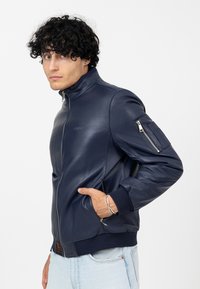 Veste en cuir bleu marine avec un col montant, fermeture éclair et poche zippée sur le bras. Poignets et ourlet côtelés. Texture lisse.