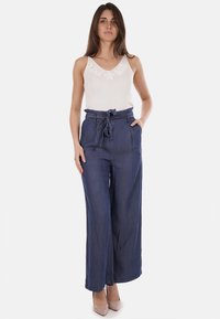 Pantaloni in denim a gamba larga con vita alta e cintura, caratterizzati da una consistenza morbida e da un colore blu profondo. Abbinati a un top leggero senza maniche.