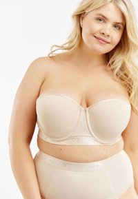 Beige strapless beha met voorgevormde cups en beugel, vervaardigd uit satijnachtige stof en voorzien van een elastische band met logo. Gecombineerd met bijpassende high-waisted slip.
