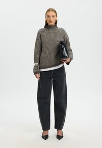 Maglione grigio oversize con motivo a chevron, jeans neri vita alta, décolleté nere a punta e borsa nera strutturata. Tessuto liscio, vestibilità casual.