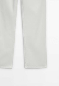 Partie inférieure d'un pantalon gris clair à coupe droite sur fond blanc montrant les détails de l'ourlet et de la couture latérale.