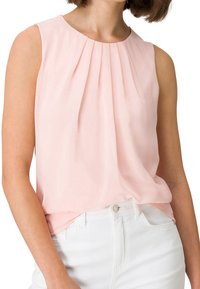 Blusa sin mangas de color rosa pálido con diseño plisado, hecha de tela ligera; llevada sobre jeans blancos con cierre frontal de botones.