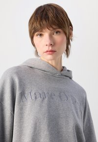 Grå hettegenser med brodert tekst "Marc O'Polo", med avslappet passform og mykt bomullsblandingsmateriale. Detaljer inkluderer en hette med snor.