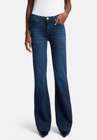 Donkerblauwe flared jeans van denim. Ze hebben een klassiek vijf-pocketdesign en een knoopsluiting. Gladde textuur met nette stiksels.