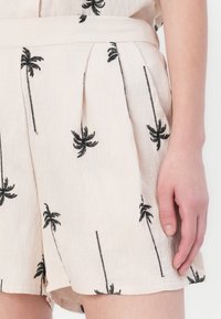 Shorts beige clair en tissu texturé, ornés d'une broderie de palmiers noirs et de plis à la taille pour un ajustement décontracté.