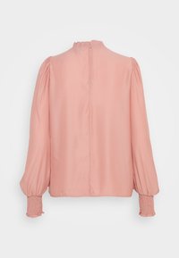Blouse rose à manches longues avec poignets froncés, épaules bouffantes et petit col à volants, vue de dos avec une fermeture éclair centrale.