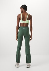 Reggiseno sportivo verde chiaro con spalline regolabili e schienale basso. Leggings svasati verde scuro con una vita alta e logo sul retro.