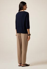 Un pull marine avec des manches ¾ associé à un pantalon beige clair, ample. Design simple avec une silhouette décontractée, porté avec des ballerines noires.