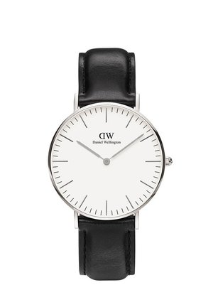 Minimalist wristwatch with white dial, silver hour and minute hands, black leather strap, and Daniel Wellington logo at top center.