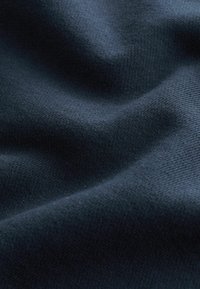 Tissu tricoté bleu foncé avec une texture visible et des plis doux créant des ombres et des lumières délicates.