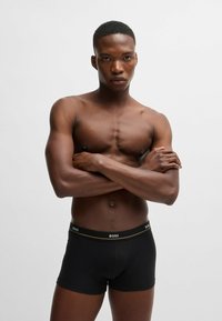 Zwarte boxershorts met een gouden accent op de tailleband waarop het "BOSS"-logo staat. Soepele stof, strakke pasvorm en een lengte tot midden boven de dij. Huid zichtbaar erboven.