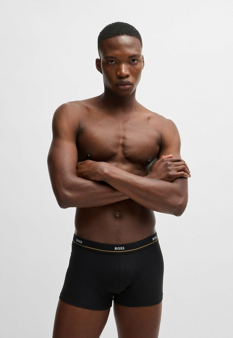 Zwarte boxershorts met een gouden accent op de tailleband waarop het "BOSS"-logo staat. Soepele stof, strakke pasvorm en een lengte tot midden boven de dij. Huid zichtbaar erboven.