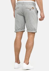 Szare bawełniane szorty z podwiniętymi nogawkami, dwoma tylnymi kieszeniami z guzikami i skórzaną naszywką na pasku. Widoczne białe sneakersy.