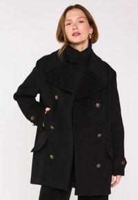 Cappotto nero doppio petto realizzato in misto lana; presenta grandi rever, due tasche frontali e bottoni color oro. Tessuto strutturato visibile.