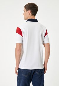 Hvid polo t-shirt med navy krave og røde detaljer på skuldrene. Blødt bomuldsstof, korte ærmer og løs pasform. Bæres med mørke denim jeans.