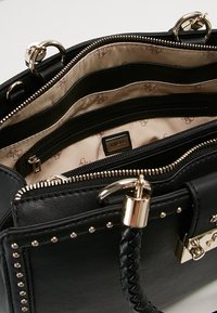 Sac à main synthétique noir avec quincaillerie dorée, plusieurs compartiments, doublure intérieure à motif et accent de poignée tressée. Présente des détails cloutés.