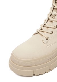 Beżowy skórzany botek za kostkę o teksturowanej powierzchni, z grubą platformą i złotymi przelotkami. Posiada sznurowanie i wzmocniony nosek.