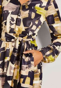 Satin-Kleid mit langen Ärmeln in einem abstrakten Muster aus Dunkelblau, Creme und Grün. Es verfügt über ein Wickeldesign und ein gebundenes Gürteldetail in der Taille.