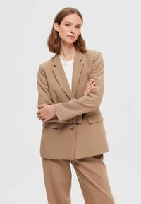 Overdimensioneret beige blazer med en struktureret design, spidse lapeller, to frontlommer og knaplukning. Lavet af tekstureret stof.