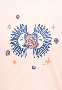 Δύο στυλιζαρισμένοι ήλιοι με πρόσωπα πλαισιώνουν έναν κεντρικό κύκλο που περιέχει το κείμενο «Santa Cruz», περιβαλλόμενο από μικρούς πλανήτες και αστέρια σε ανοιχτό φόντο.