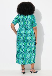 Grün-blaß gemustertes Midi-Kleid mit kurzen Ärmeln und einem Bindeband in der Taille, kombiniert mit blauen Absatzsandalen. Sanfte Textur und fließendes Design.