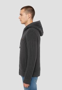 Pull à capuche gris foncé avec texture côtelée, manches longues et poche zippée. Design décontracté, adapté à diverses occasions.