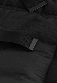 Sort stof med en tekstureret overflade, der har sorte webbingremme og plastikhardware. Overfladen viser små variationer i tekstur.