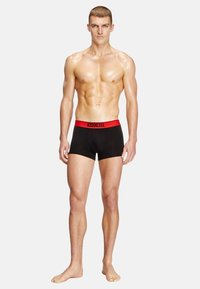 Boxers noirs avec une ceinture élastique rouge portant l'inscription "DIESEL". Fabriqués en tissu doux, de design ajusté et de longueur mi-cuisse.