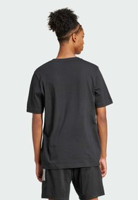 T-shirt di cotone nera con maniche corte, collo a giro, e vestibilità rilassata, vista da dietro, abbinata a pantaloncini neri.