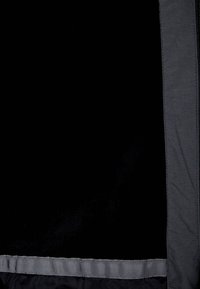 Černá látka s hladkým povrchem, která má šedou podšívku a žebrovaný prvek na spodním okraji. Jednoduchý design s minimem detailů.