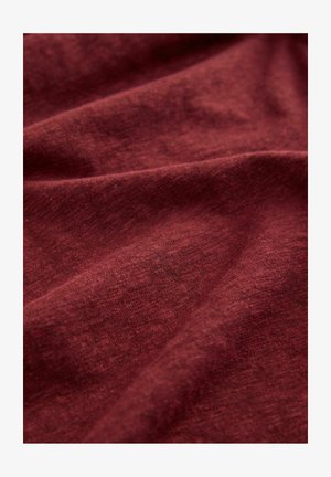 Tissu en coton bordeaux avec une finition texturée, présentant de douces ondulations et un aspect légèrement chiné, indiquant flexibilité et confort.