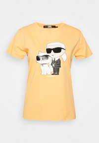 Żółta bawełniana koszulka z grafiką postaci i kota w czarnych okularach przeciwsłonecznych, o prostych liniach i minimalnych detalach.