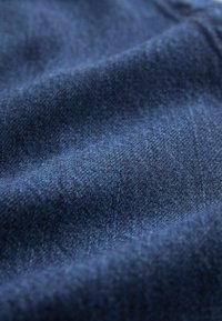 Tummansinistä farkkukangasta, jossa on pehmeä rakenne ja hienovarainen kiilto. Materiaalissa on tiheä kudonta ja näkyviä ompelualueita.